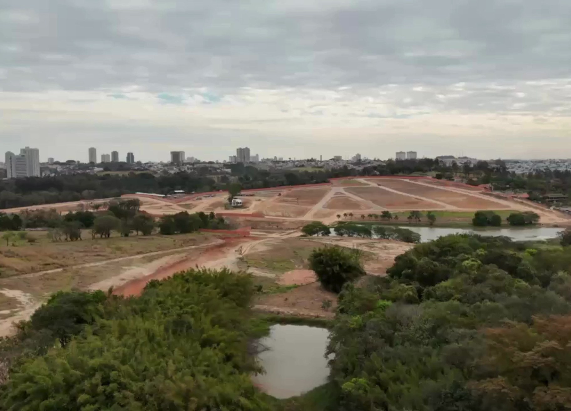 Vista aérea das obras do Loteamento Jardim Hípica em Indaiatuba, com quadras demarcadas, terraplanagem e lago natural.